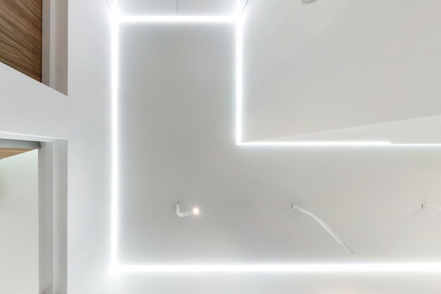 Mirando hacia arriba en el techo suspendido con lámparas halógenas y construcción de paneles de yeso en una habitación vacía en un apartamento o casa Techo tensado blanco y forma compleja