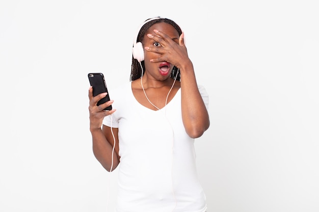 mirando conmocionado, asustado o aterrorizado, cubriendo la cara con la mano con auriculares y un teléfono inteligente