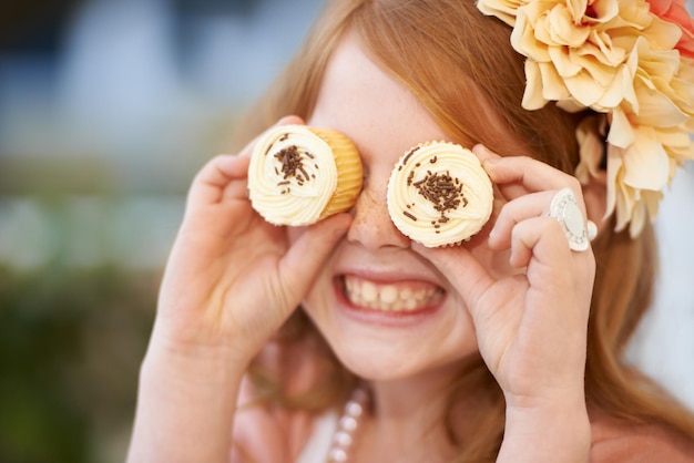 Mirando dulce Una niña juguetonamente sosteniendo cupcakes frente a sus ojos