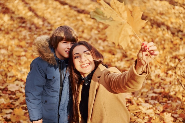 Mirando la hoja Madre con su hijo se está divirtiendo al aire libre en el bosque de otoño