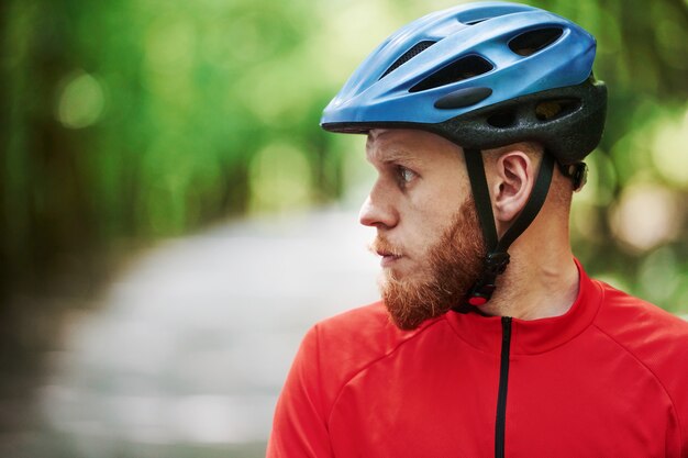 Mirando hacia un lado. Ciclista en bicicleta está en la carretera asfaltada en el bosque en día soleado