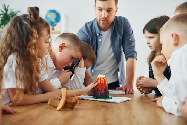 Mirando el modelo del volcán Grupo de niños estudiantes en clase en la escuela con el maestro