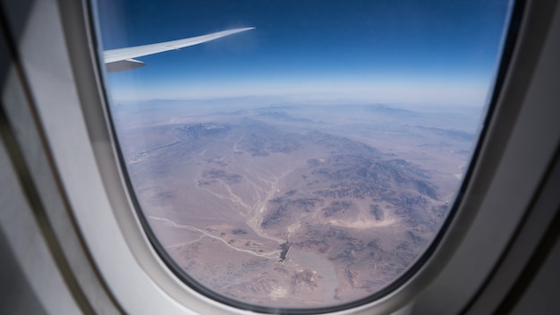 Mirando a través de la ventana del avión viendo el ala del avión y el postre de Dubai con el cielo azul