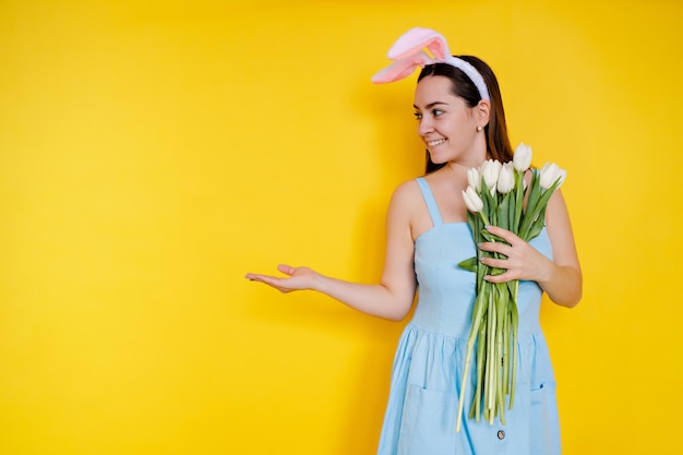 Mire aquí Retrato de una hermosa joven con orejas de conejo el día de Pascua sosteniendo una flor