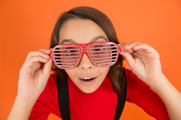 Mire con interés. tienda de moda de gafas. accesorio de fiesta.  divirtiéndose. fiesta de carnaval. gafas de niño y de rayas. chica con  anteojos fondo naranja. evento y entretenimiento. celebración de fiestas.