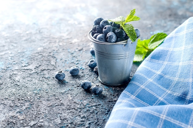 Mirtilos de frutas maduras em um mini balde com folhas de hortelã em um fundo escuro