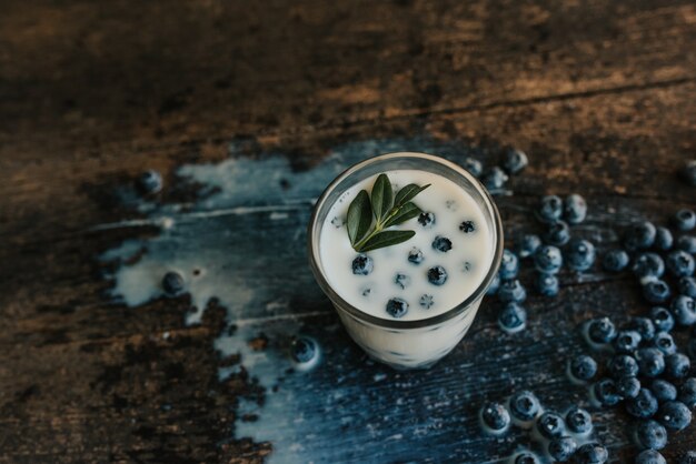 Mirtilos flutuam em um copo transparente com leite. Folhas verdes de manjericão em um copo. Azul fresco