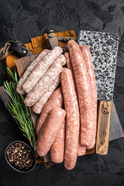 Mischen Sie frische Rohwürste Rindfleisch, Schweinefleisch, Lammfleisch und Hühnerhackfleischwürste auf einem Metzger-Schneidebrett mit Gewürzen Schwarzer Hintergrund Ansicht von oben