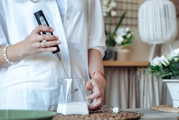 Mischen von Milch im Glastopf durch Aufschäumer closeup Weibliche Herstellung von schaumiger Milch mit Handmixer Hausfrau Frau in Heimkleidung mit Mixer Peitschen