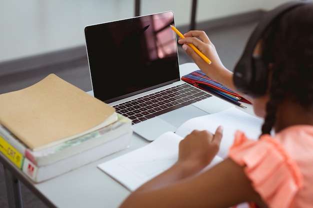 Mischlingsschülerin im Klassenzimmer mit Kopfhörern und Laptop, mit Platz für Kopien auf dem Bildschirm