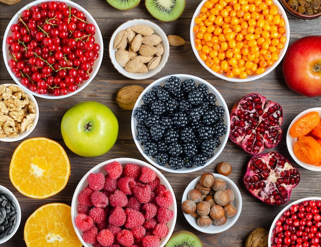 Mischung aus frischen beeren, nüssen und früchten. gesundes essen enthält viele vitamine und nützliche spurenelemente. brauner hölzerner hintergrund.