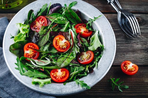 Mischung aus frischen grünen Salatblättern mit Arugulasalat, Spinatrüben und Tomaten auf rustikalem Holzhintergrund