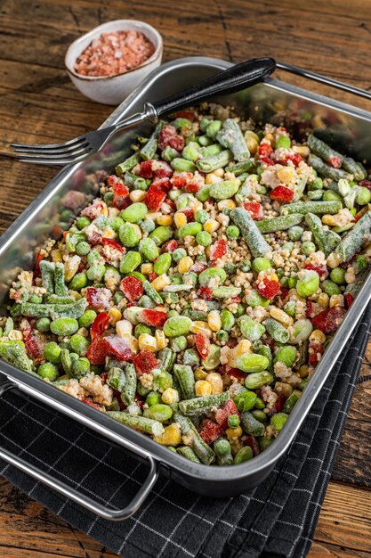 Mischung aus gefrorenem rohem Gemüse und Quinoa in einem Küchentablett Holzhintergrund Draufsicht