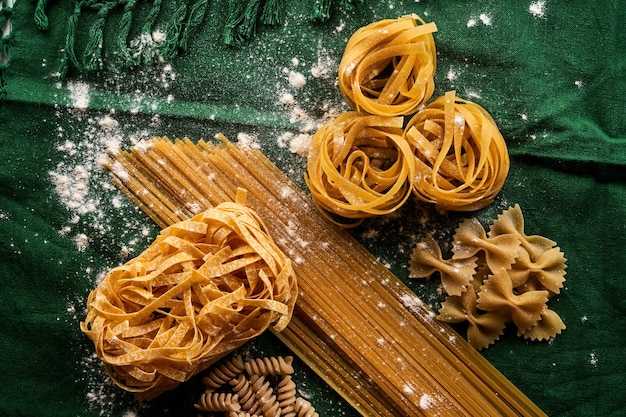 Mischung aus verschiedenen Pastasorten auf grünem Stoffhintergrund, verschiedene Makkaroni-Konzepte kochen
