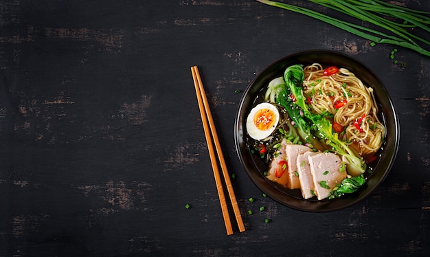 Miso-Nudeln mit Ei, Schweinefleisch und Pak Choi Kohl in der Schüssel auf dunklem Tisch.