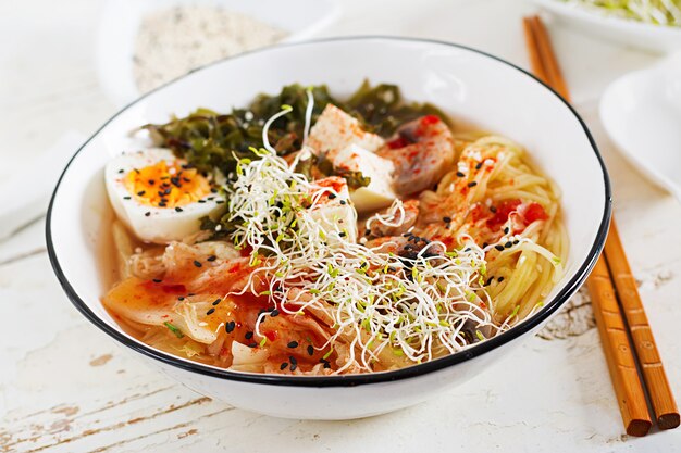 Miso Ramen Fideos asiáticos con col kimchi, algas, huevo, champiñones y queso tofu en un tazón en la mesa de madera blanca.