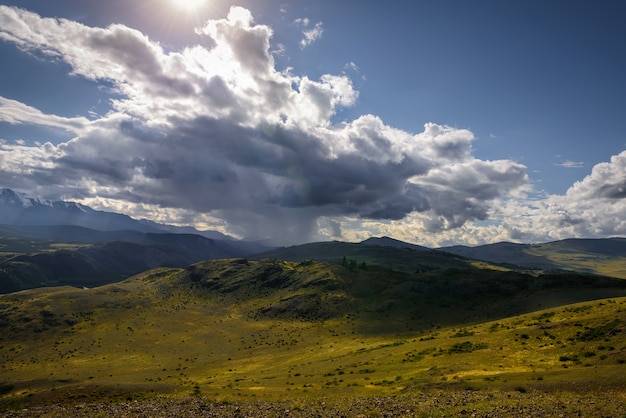 Misterioso paisaje de montaña con colinas de nubes de tormenta y rayos del sol.