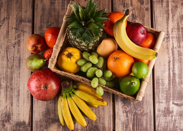 Mistura de frutas tropicais exóticas coloridas e suculentas frescas em uma cesta na vista superior do plano de fundo de madeira