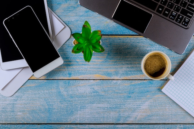 Mistura de material de escritório com aparelhos de telefone inteligente trabalhando em um computador laptop em uma xícara de café em um fone de ouvido sem fio