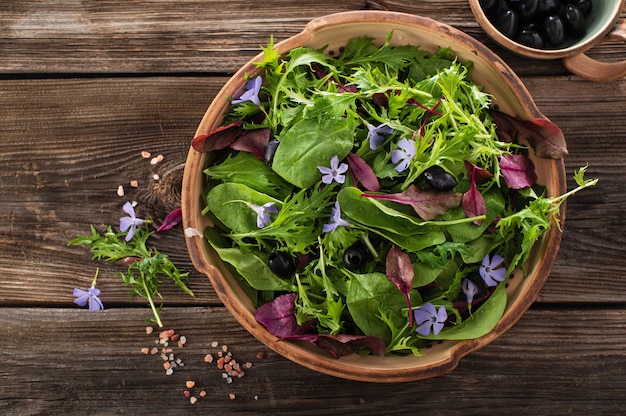 Mistura de salada com salada de mizuna de espinafre bebê com flores e azeitonas em um fundo de madeira