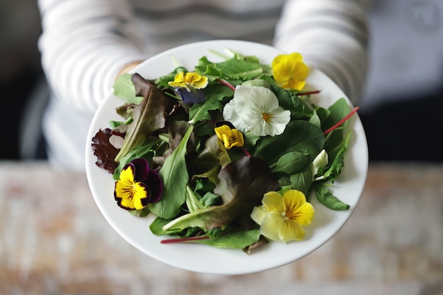 Mistura de saladas com flores em um prato branco, realizada por uma menina