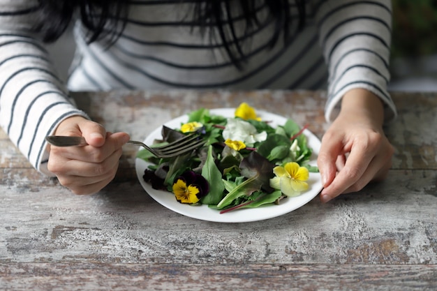 Mistura de saladas com flores em um prato branco, realizada por uma menina