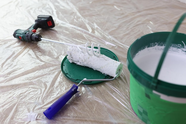Misturador de tinta com balde de tinta branca e escova de rolo na pintura e melhoria da casa no chão