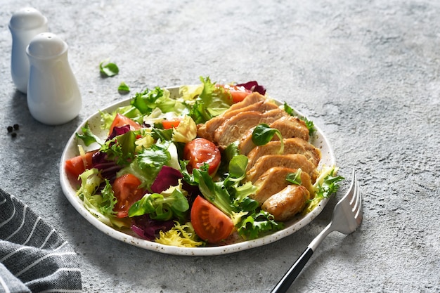 Misture a salada com tomate e filé de frango em um prato.