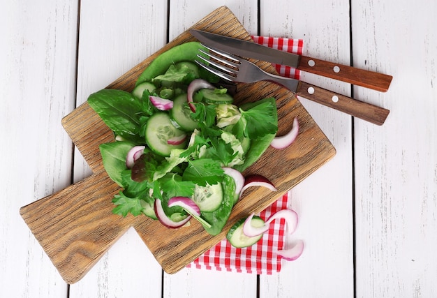 Misture folhas de salada com pepino e cebola em fatias na prancha de corte e colorir as tábuas de madeira de fundo