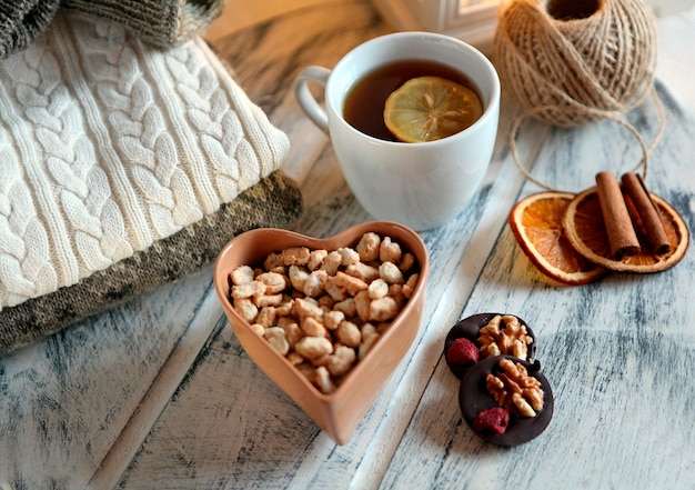 Misture nozes, frutas secas e chocolate com xícara de chá e suéter na mesa branca conceito de inverno