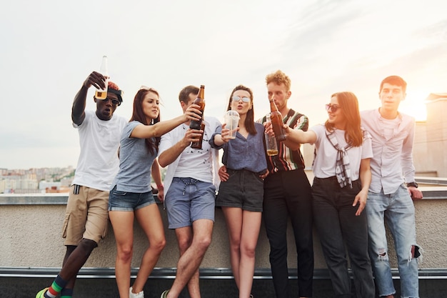 Mit Alkohol am Rand des Daches stehend Eine Gruppe junger Leute in Freizeitkleidung feiert tagsüber zusammen