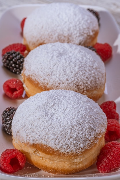 Mit Berliner Gelee gefüllter Donut mit Himbeere und Brombeere auf hölzernem Hintergrund.