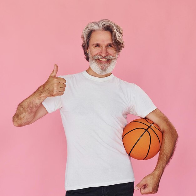 Mit dem Sportball in den Händen Stilvoller moderner älterer Mann mit grauen Haaren und Bart ist im Inneren