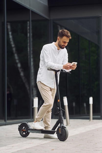 Mit dem Telefon Stilvoller Mann ist tagsüber mit seinem Roller im Freien