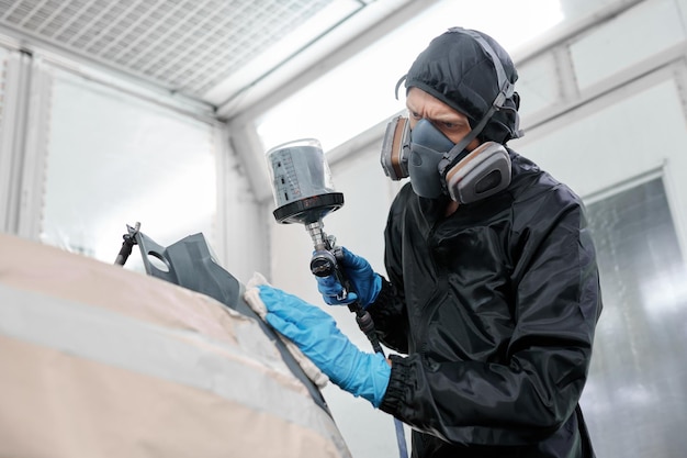 Foto mit der präzision einer lackierkammer verleiht ein handwerker in einem schwarzen overall und einer atemschutzmaske dem auto ein atemberaubendes finish