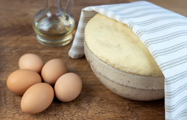 Mit einem Handtuch bedeckter Hefeteig zum Backen von selbstgebackenem Brot auf einem Holztisch