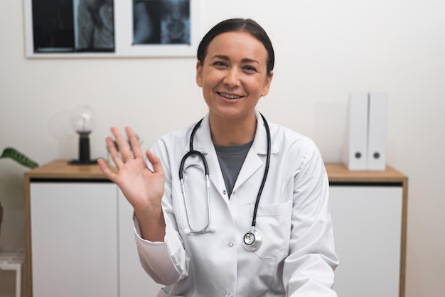 Mit einem Lächeln winkt eine Arztin während eines Online-Aufenthalts mit der Hand zur Kamera