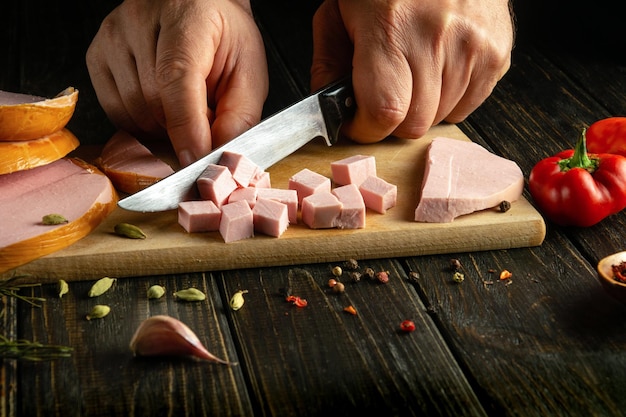 Mit einem Messer in den Händen eines Kochens verbrannte Würstchen schneiden, um ein köstliches Mittagessen auf dem Küchentisch zuzubereiten