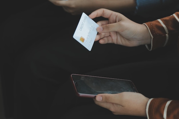 Mit einer Kreditkarte in den Händen einer jungen Geschäftsfrau wird ein Geschäft auf einem Mobiltelefon und auf einem Schreibtisch mit Laptop bezahlt
