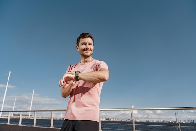 Mit einer Smartwatch sieht ein Läufer in Fitnesskleidung aus, wie ein Mann Sport treibt, ein glücklicher Athlet ist eine Person