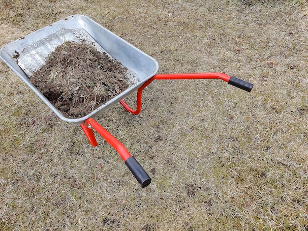 Mit Erde oder Kompost gefüllte Gartenschubkarre am Hof Saisonale Gartenreinigung vor dem Herbst Gartenwagen aus Metall mit Erde auf dem RasenWagen mit Erde