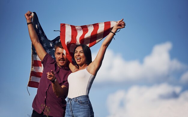 Mit erhobenen Händen. Fühlt Freiheit. Schöne Paare mit amerikanischer Flagge haben eine gute Zeit im Freien im Feld.