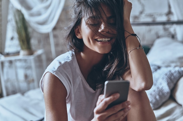 mit Freund chatten. attraktive junge Frau, die Smartphone benutzt und Hand im Haar hält