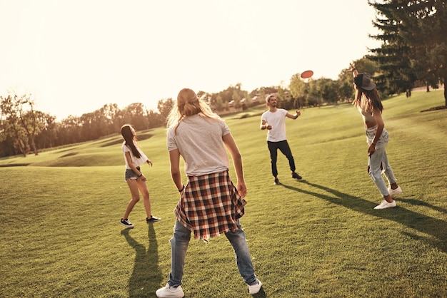 Mit Freunden Spaß haben. Voller Länge junger Leute in Freizeitkleidung, die Frisbee spielen, während sie unbeschwerte Zeit im Freien verbringen