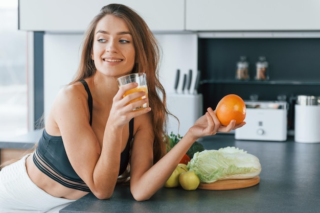 Mit frischem Orangensaft Junge europäische Frau ist drinnen in der Küche drinnen mit gesunden Lebensmitteln