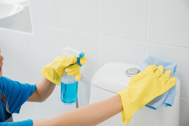 Mit gelben Gummihandschuhen wischt eine Dienstmädchen den Toilettensitz mit einem Tuch ab. Ihre Aufmerksamkeit auf Hygiene und Sauberkeit spiegelt die Essenz des sorgfältigen Haushalts und des Gesundheitskonzepts der Hausfrau wider.