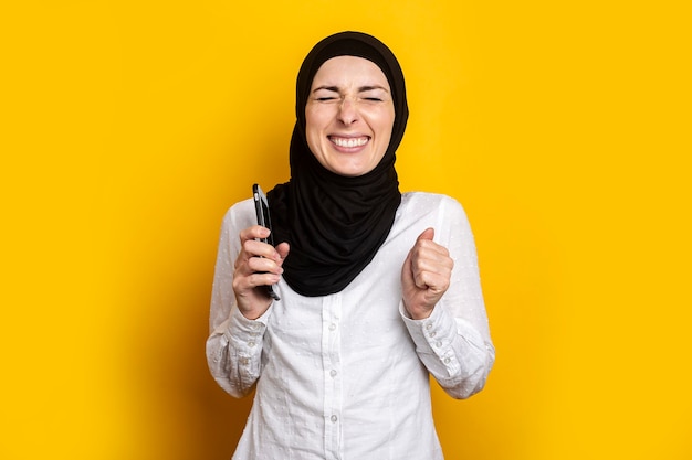 Mit geschlossenen Augen schloss eine junge Frau in einem Hijab ihre Augen mit einem Telefon auf Gelb.
