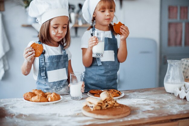 Mit Gläsern mit Milch. Familienkinder in weißer Kochuniform, die Essen in der Küche zubereiten.