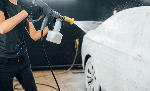 Mit Hochdruckwasser Modernes schwarzes Auto wird von einer Frau in der Autowaschanlage gereinigt