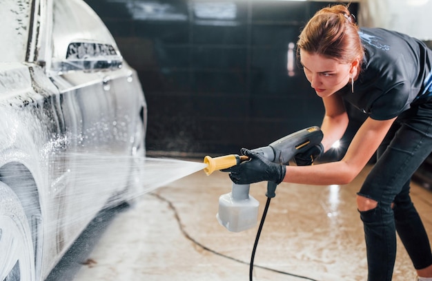 Mit Hochdruckwasser Modernes schwarzes Auto wird von einer Frau in der Autowaschanlage gereinigt